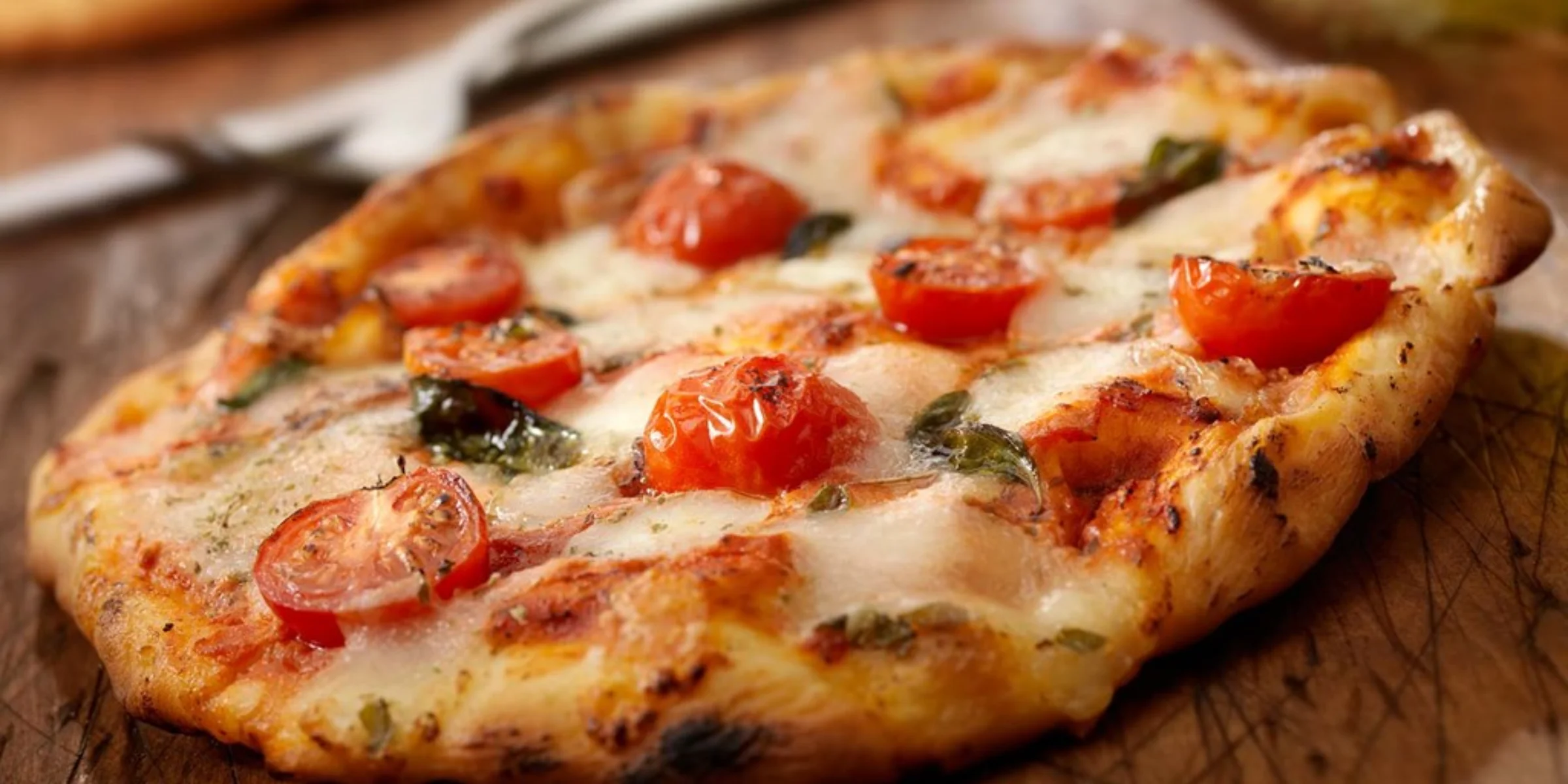 Eine frisch gebackene Pizza mit Tomaten und Basilikum auf einem Holzbrett.