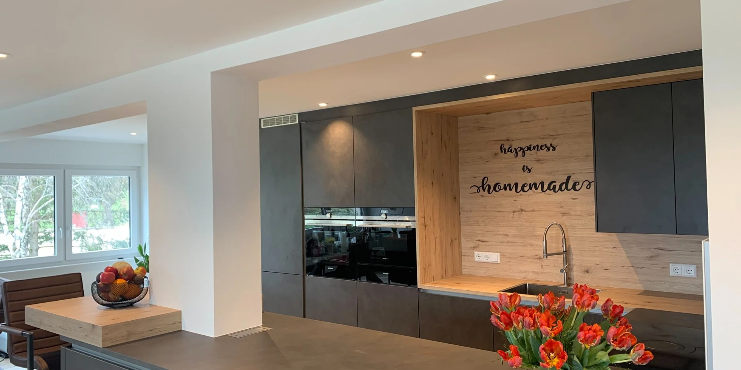 Eine moderne Küche mit dunklen Schränken und Tulpen auf der Theke, gestaltet von Nolte Küchen.