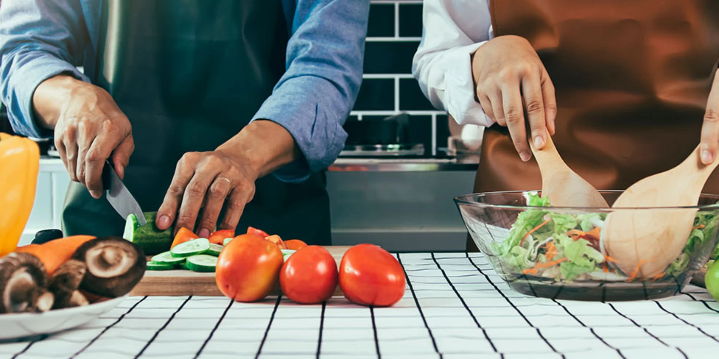 Zwei Personen bereiten gemeinsam eine Mahlzeit zu. Auf einem Küchenarbeitsplatz werden Gemüse geschnitten und ein Salat gemischt.