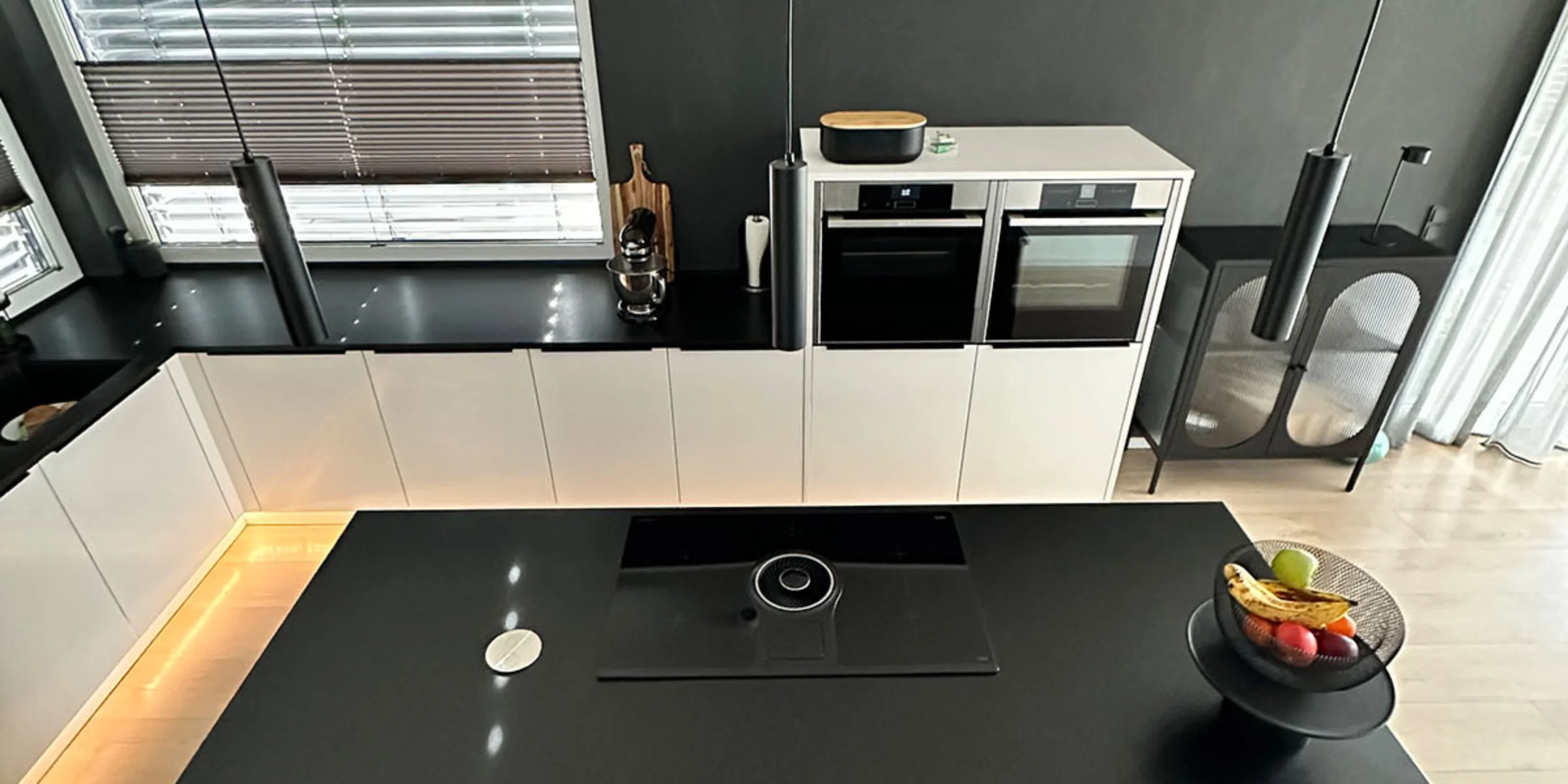 Eine moderne Küche mit schwarzer Arbeitsplatte und Kochinsel, ausgestattet von Nolte Küchen.