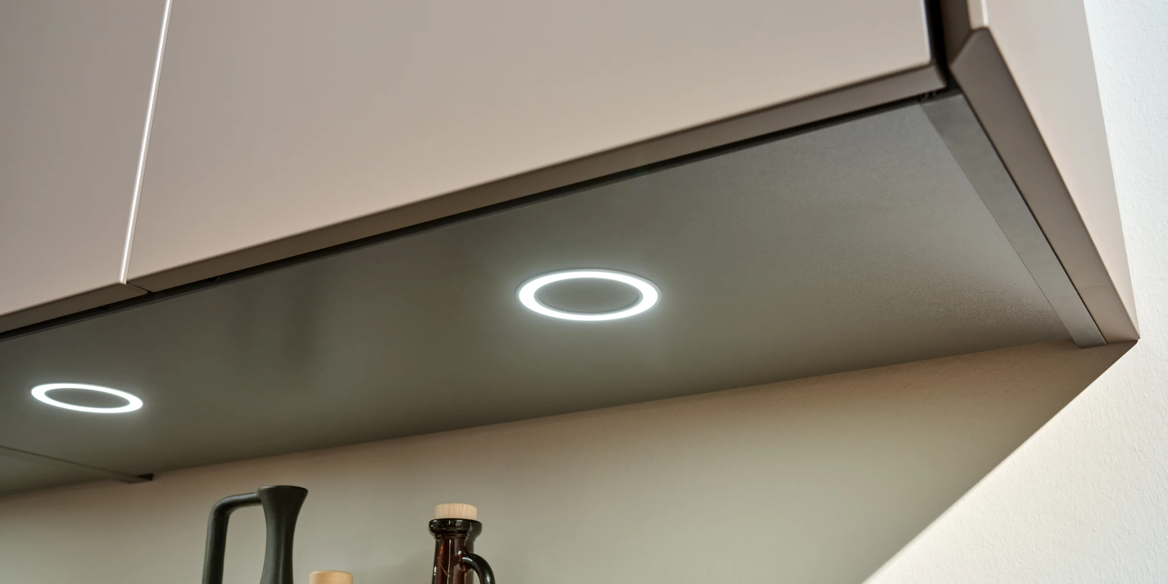 Unter einem Küchenschrank mit Beleuchtung stehen Flaschen; Nolte Küchen.