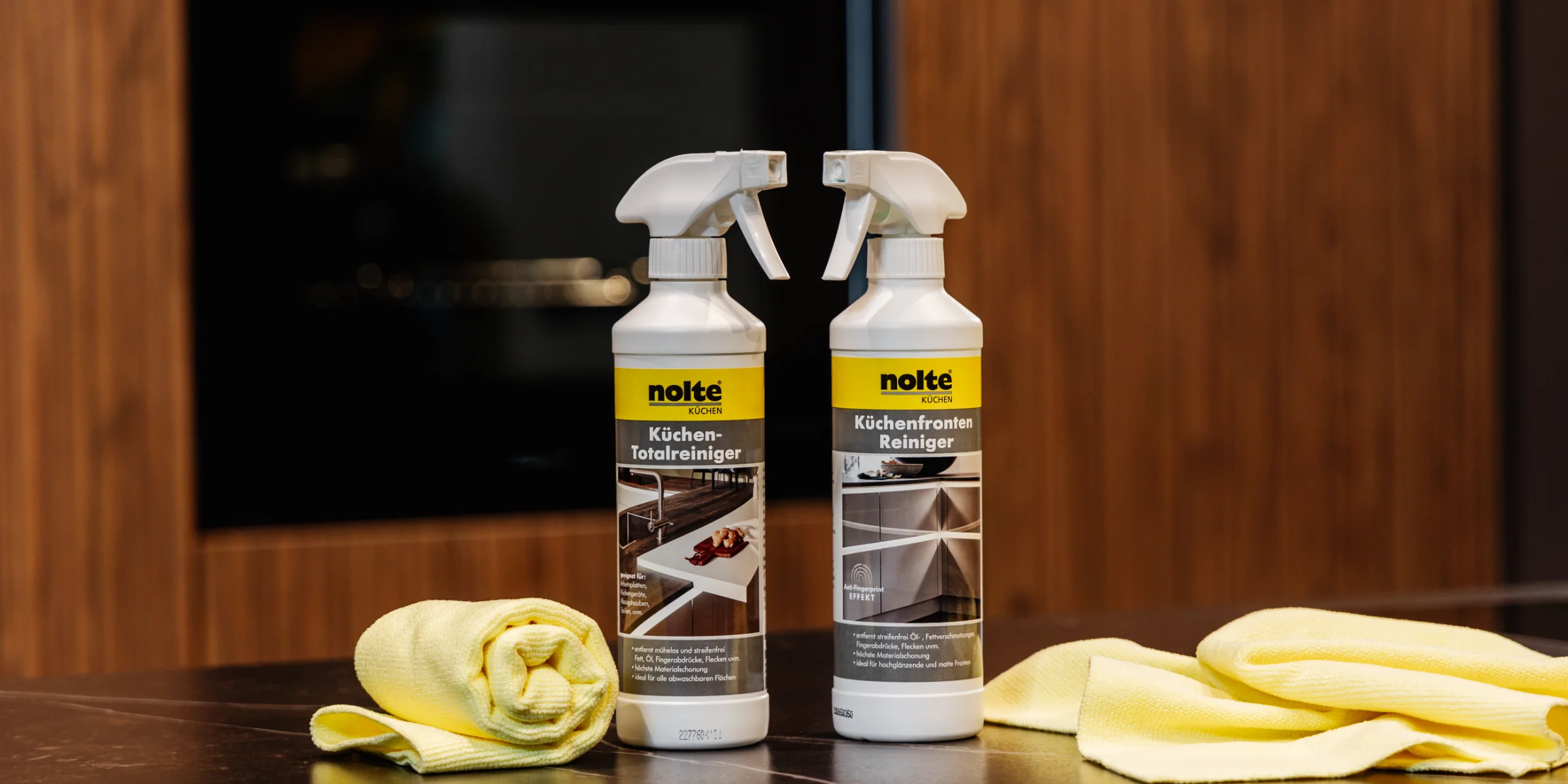 Zwei Reinigungsflaschen und gelbe Tücher auf einer Arbeitsfläche in einer Küche von Nolte Küchen.