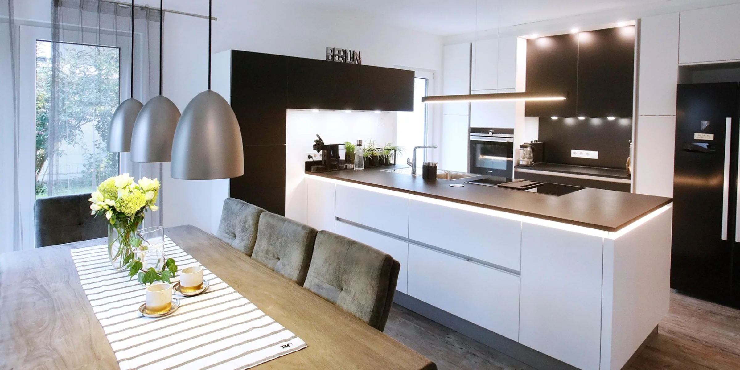 In einer modernen Küche mit Esstisch und Hängelampen präsentiert sich Nolte Küchen.