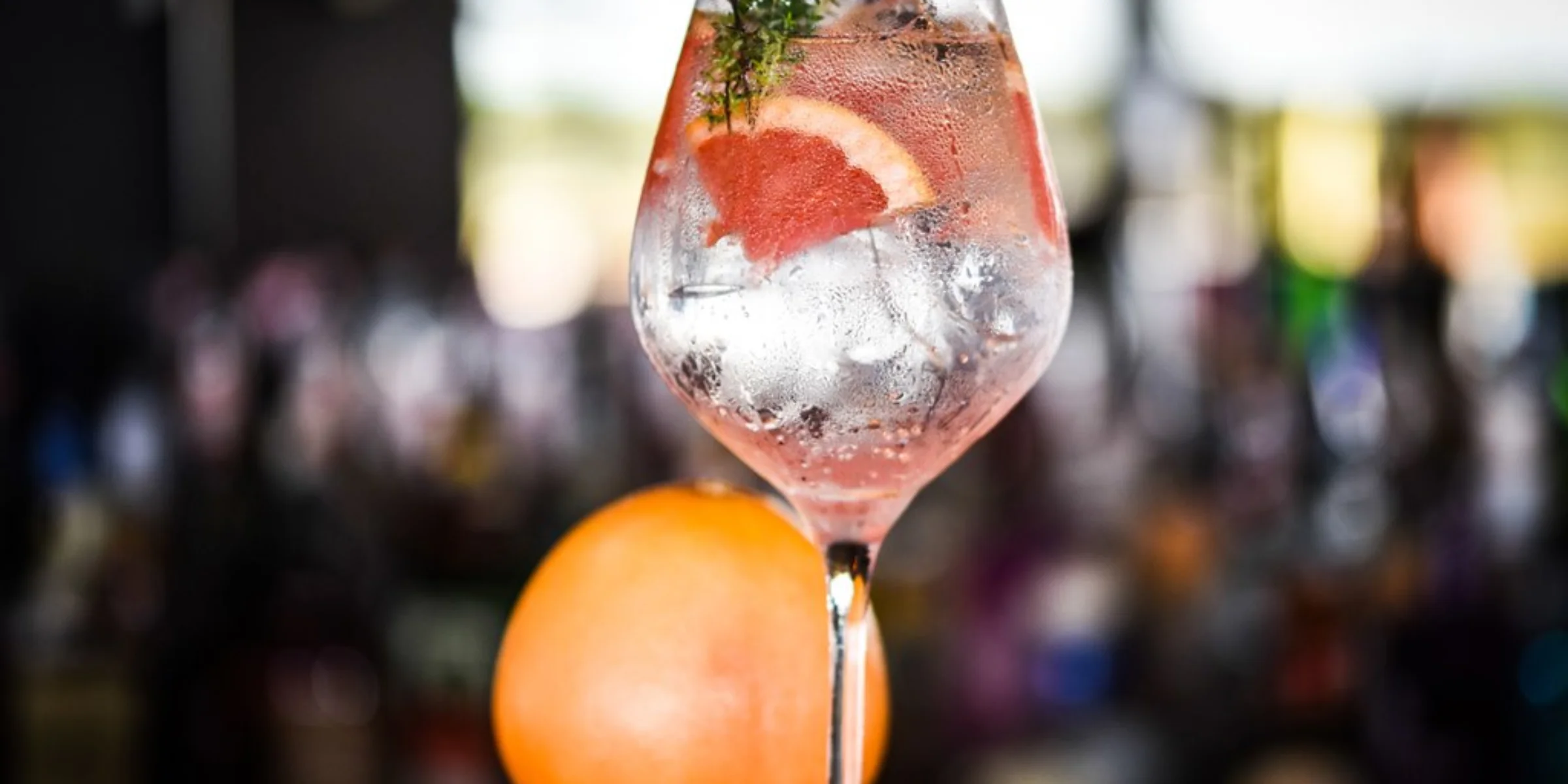 Ein Cocktailglas mit Eis, Thymianzweig und Grapefruitscheibe auf einer Theke.