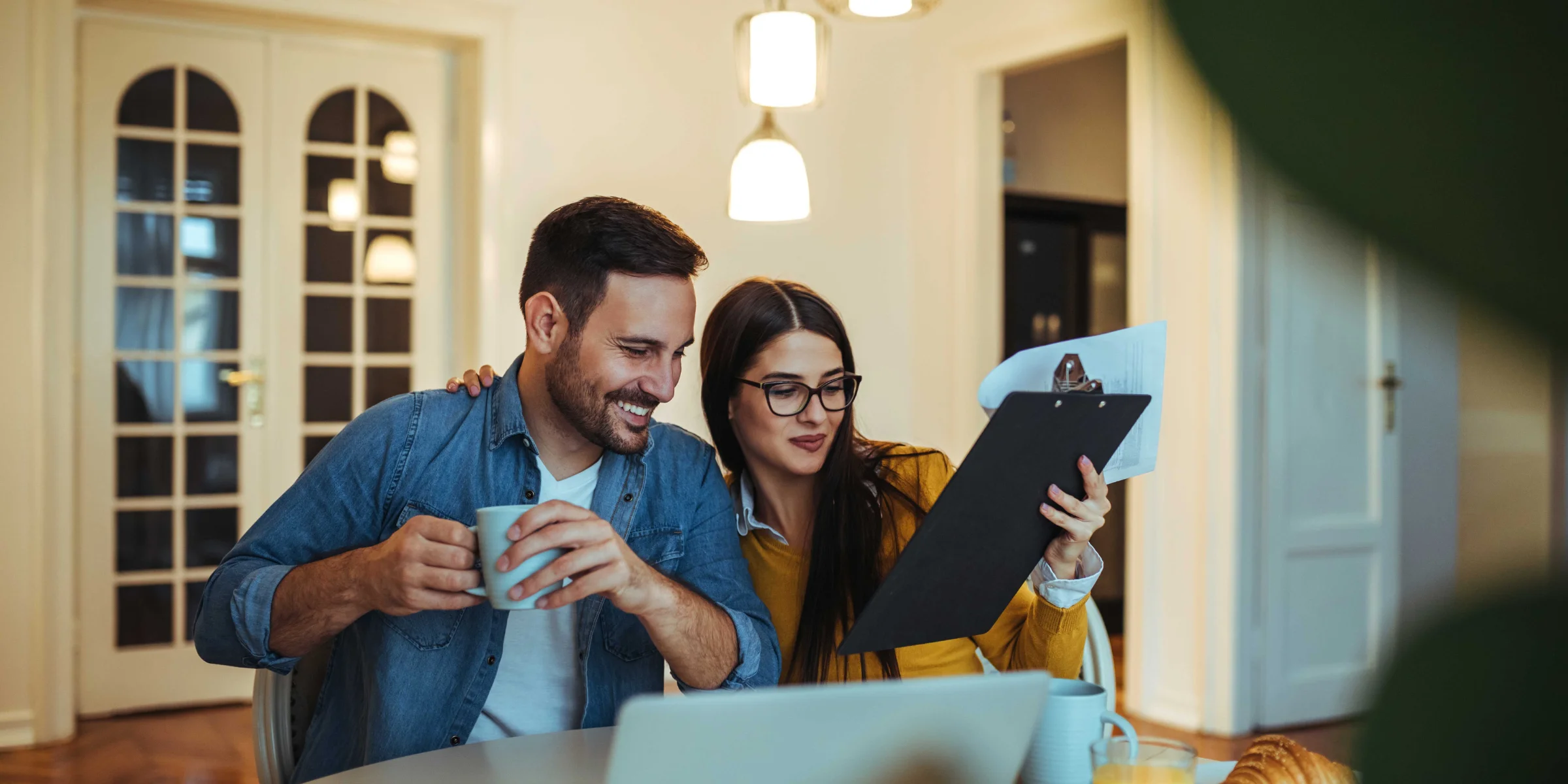 Ein Paar sitzt am Tisch beim Frühstück mit Laptop und Dokumenten.