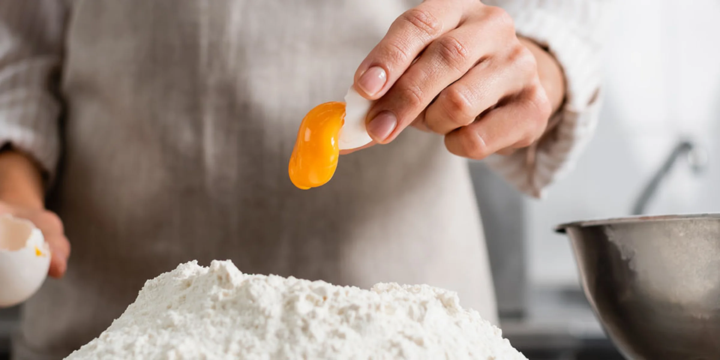 Eine Person trennt ein Eigelb über einem Mehlhaufen in einer modernen Küche von Nolte Küchen.