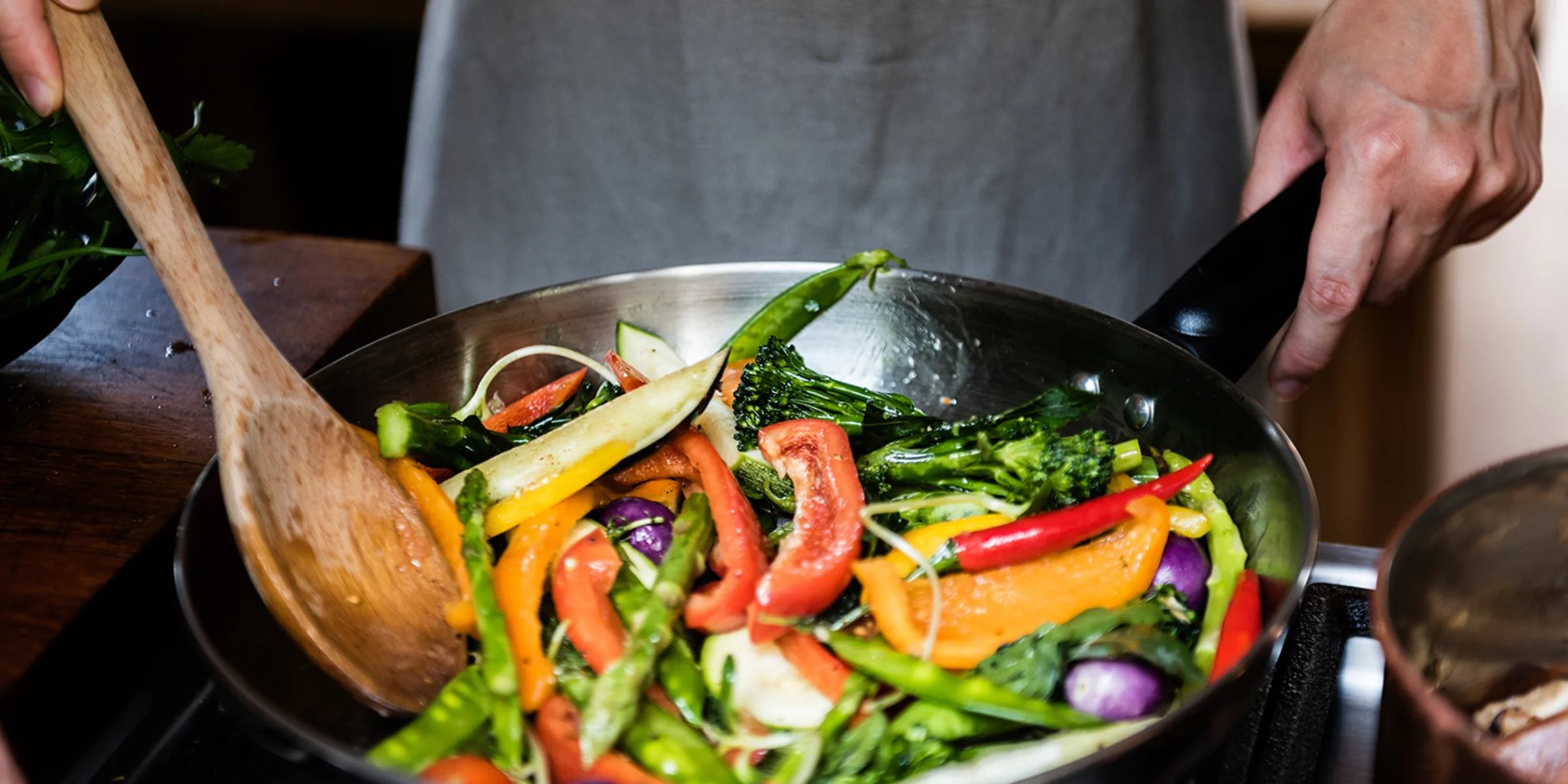 Eine Person brät buntes Gemüse in einer Pfanne.