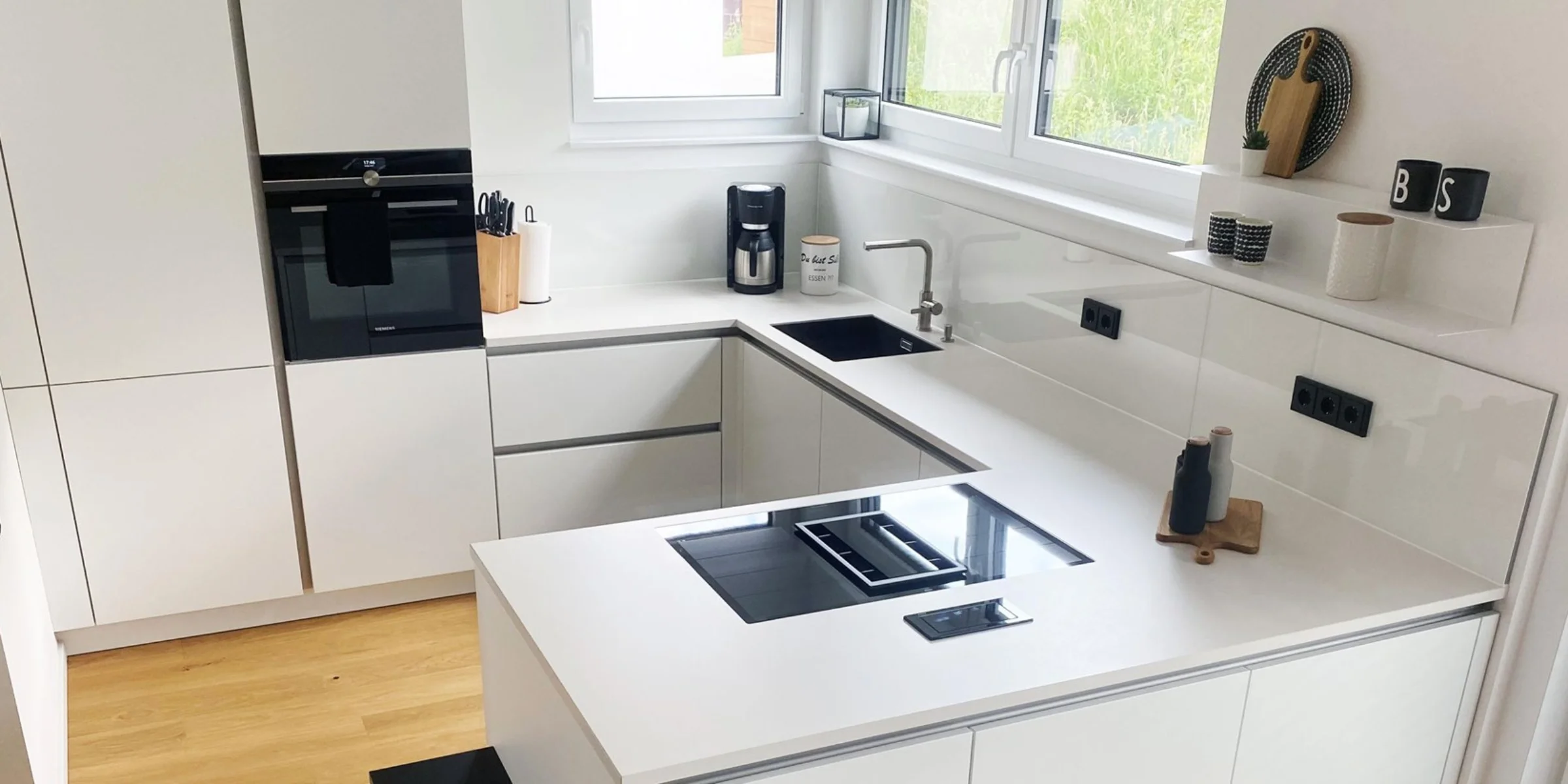 Moderne, weiße Küche mit Einbaugeräten und Eckspüle, gestaltet von Nolte Küchen.