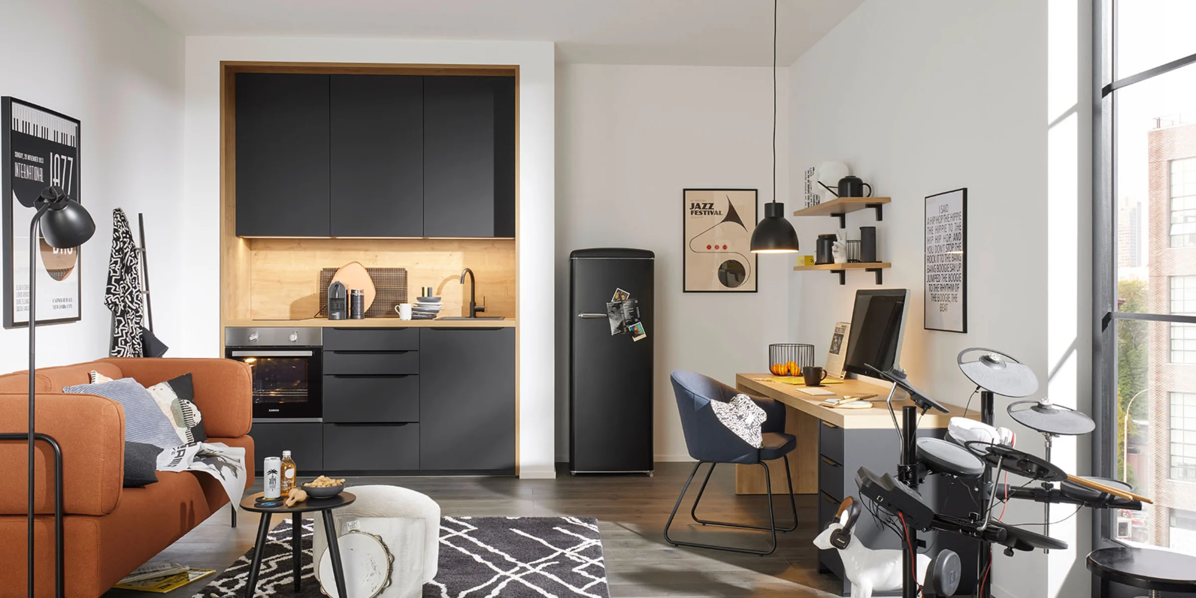 In einem modernen Raum mit grauer Küche von Nolte Küchen sind ein Sofa, ein Schreibtisch und ein elektronisches Schlagzeug zu sehen.