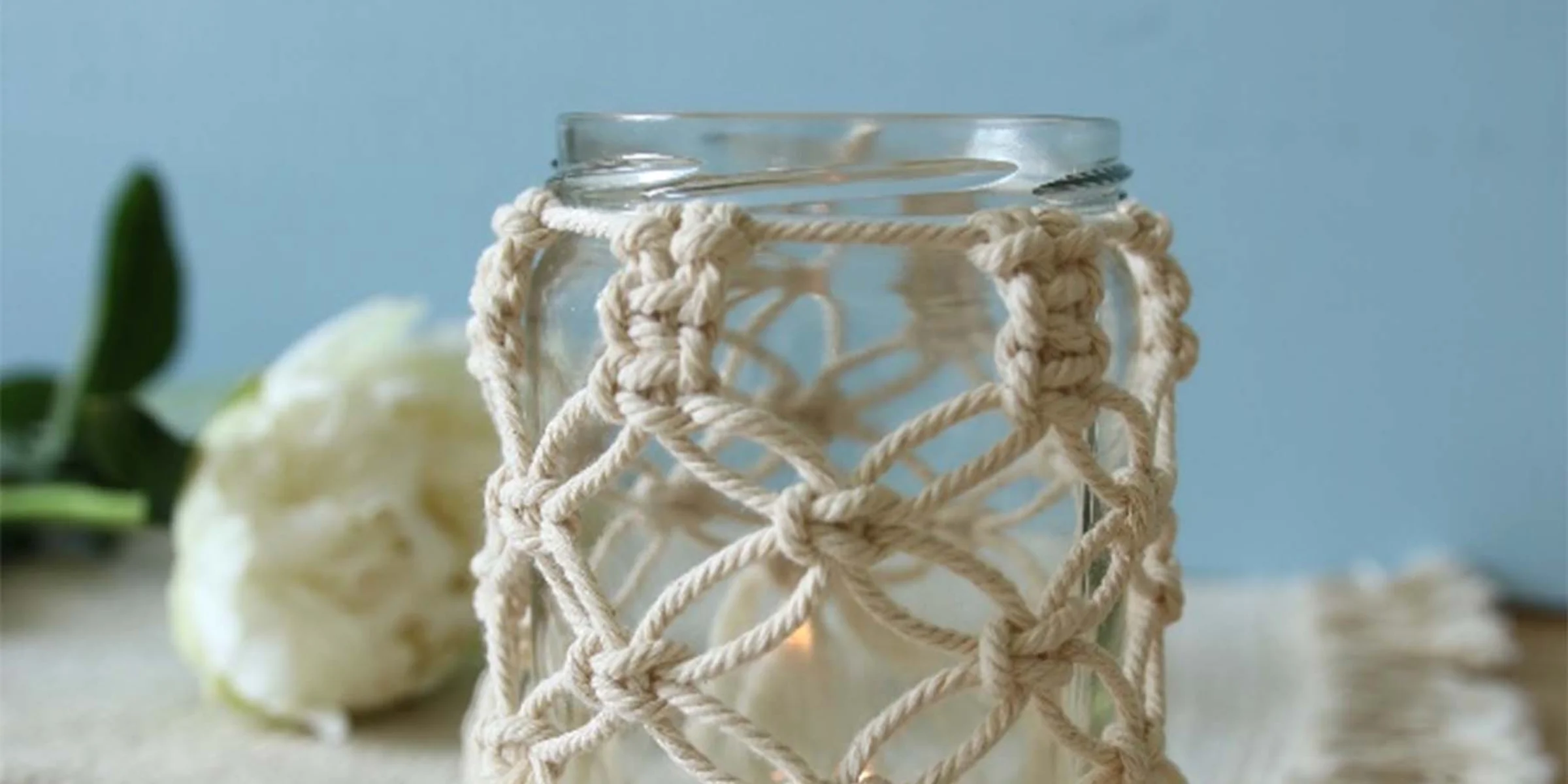 Szklanka z makramowym pokrowcem stoi na stole z frędzlowym obrusem.