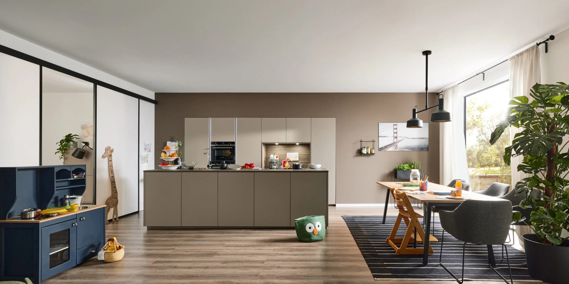 Eine moderne Küche mit Insel, Esstisch und Spielzeug in einem offenen Raum, gestaltet von Nolte Küchen.