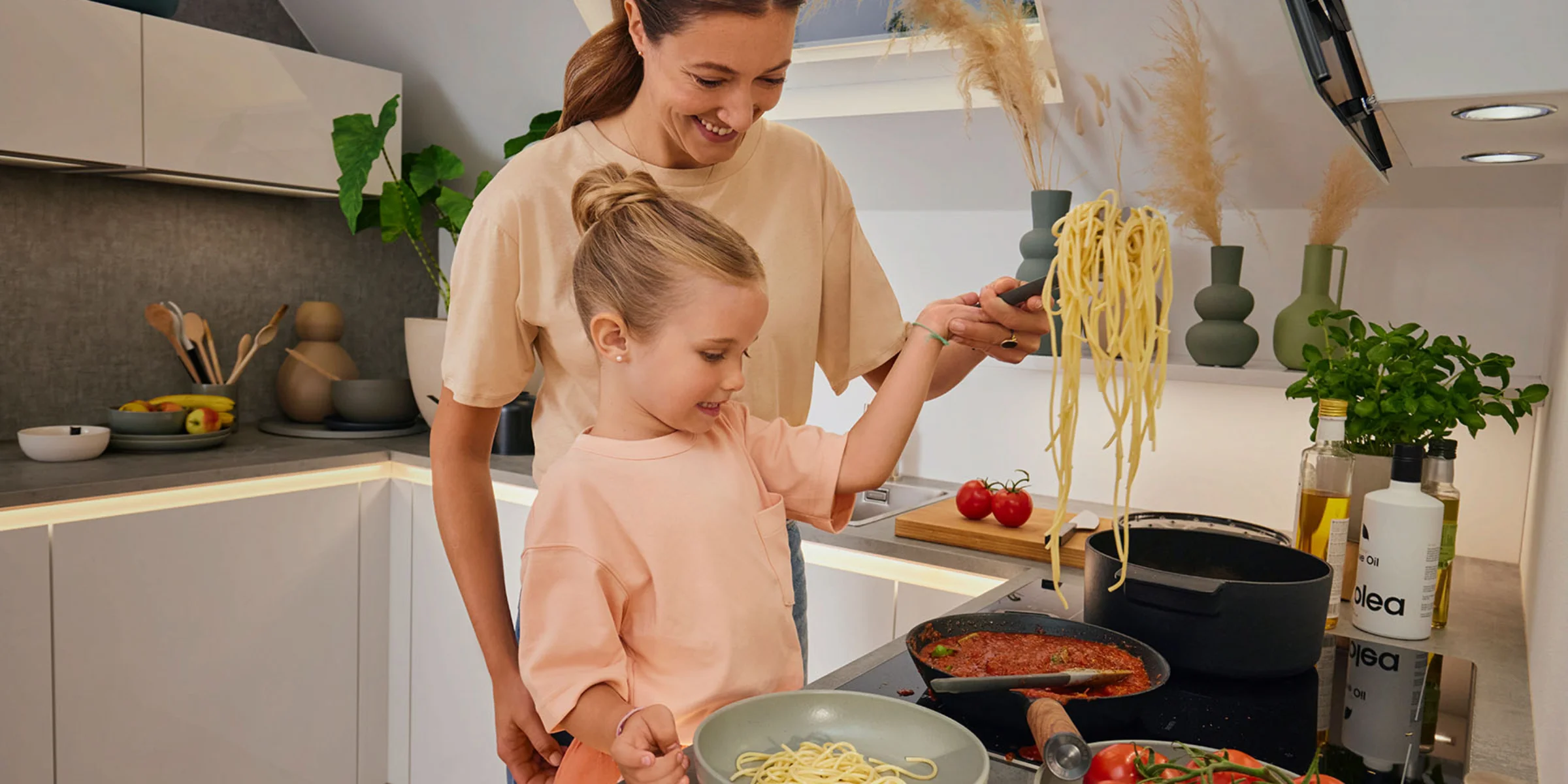 Mutter und Kind kochen gemeinsam in einer modernen Familienküche mit Kücheninsel und bereiten Pasta zu.