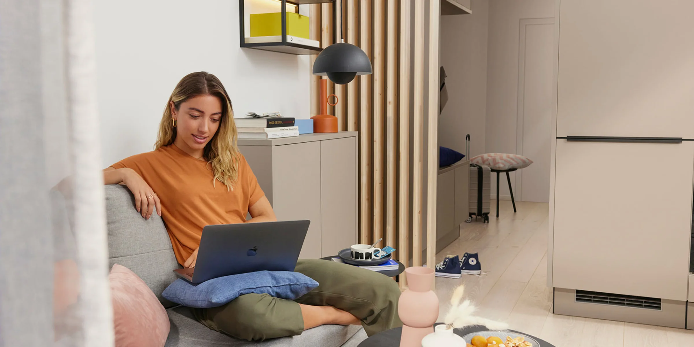 Eine Frau sitzt in einem modernen Wohnzimmer auf einem Sofa mit einem Laptop, umgeben von stilvollen Dekorationen von Nolte Living.