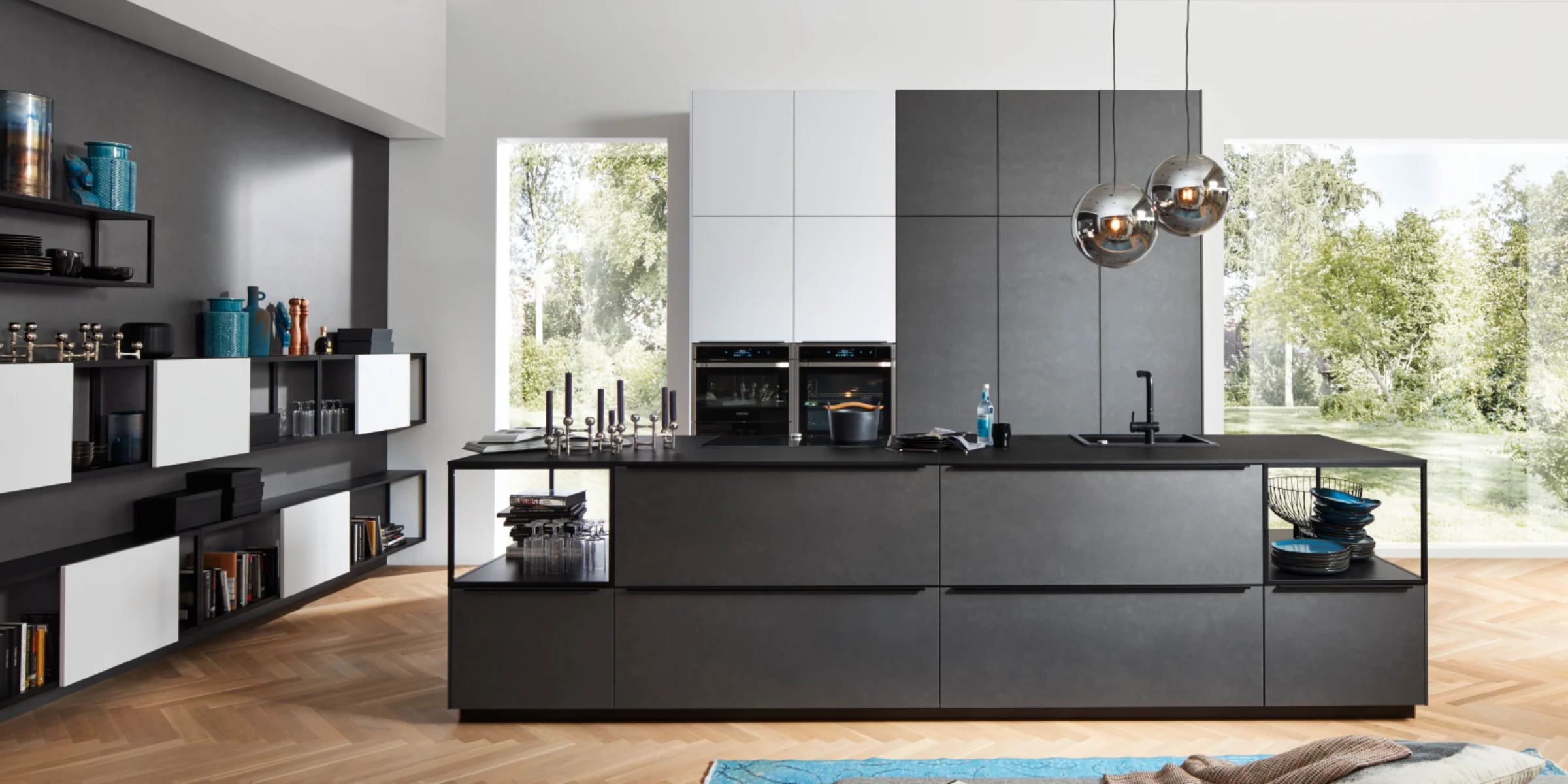 Moderne Nolte Küche mit der Front FERRO in Blaustahl und kontrastierenden Oberschränken in SOFT LACK Arcticweiß softmatt. Die grifflose Inselküche besticht durch klare Linien, offene Regale und integrierte Stauraumlösungen. Großzügige Fenster sorgen für ein lichtdurchflutetes Ambiente, das den industriellen Charakter der Blaustahl-Oberflächen stilvoll unterstreicht.