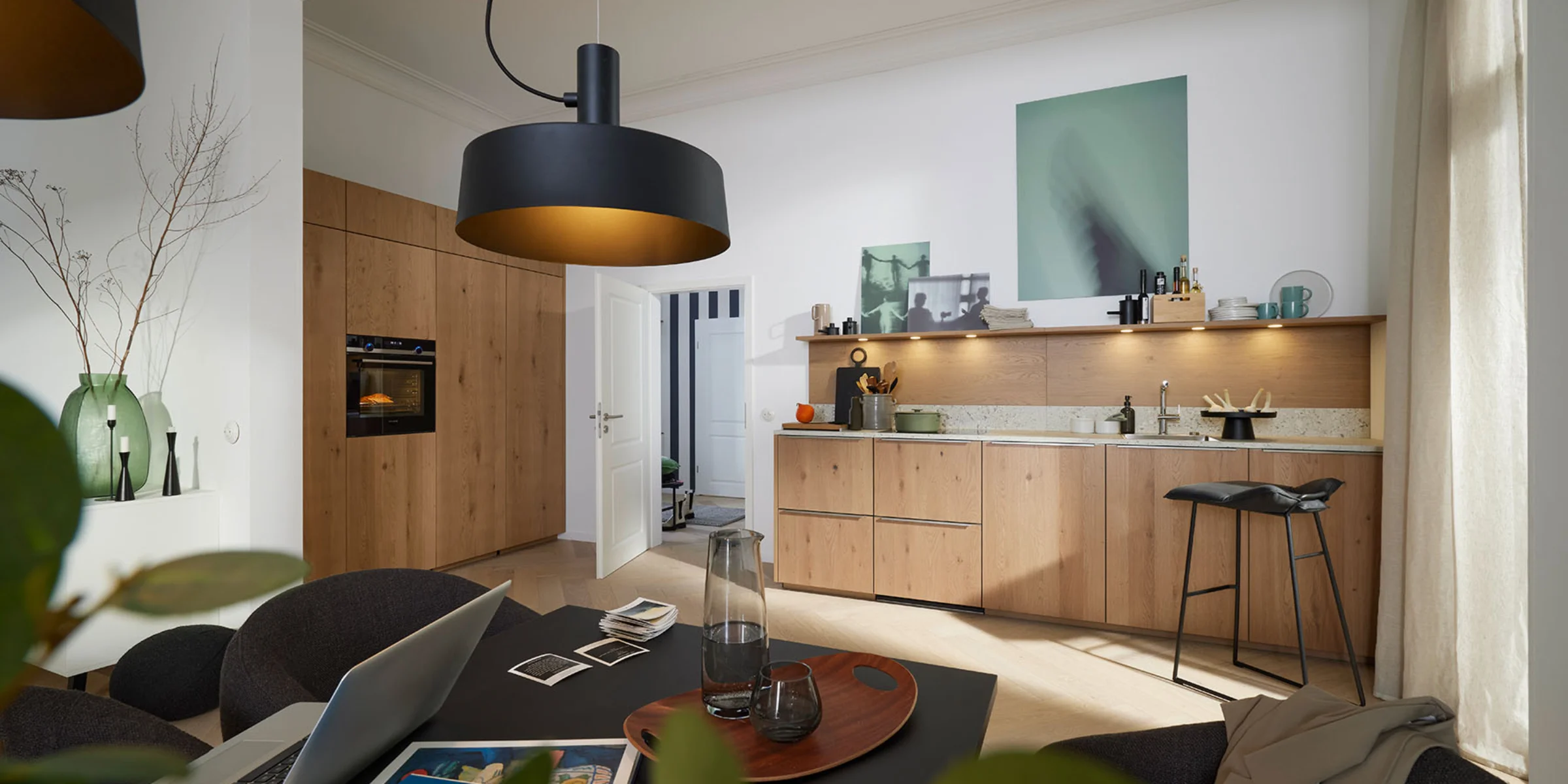 Eine moderne Küche mit Holzfronten und stilvoller Beleuchtung, im Vordergrund ein Esstisch. Nolte Küchen.