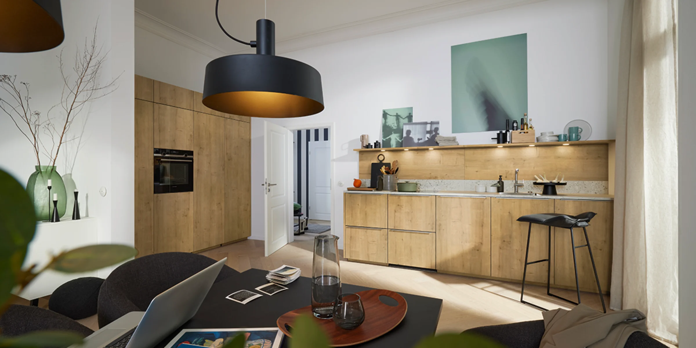 Eine moderne Küche mit Holzfronten und stilvoller Beleuchtung, im Vordergrund ein Esstisch. Nolte Küchen.