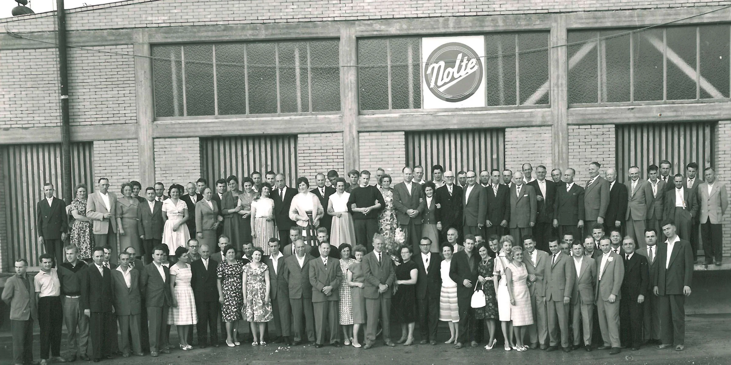 Eine große Gruppe von Menschen steht vor einem Gebäude mit einem "Nolte" Logo.