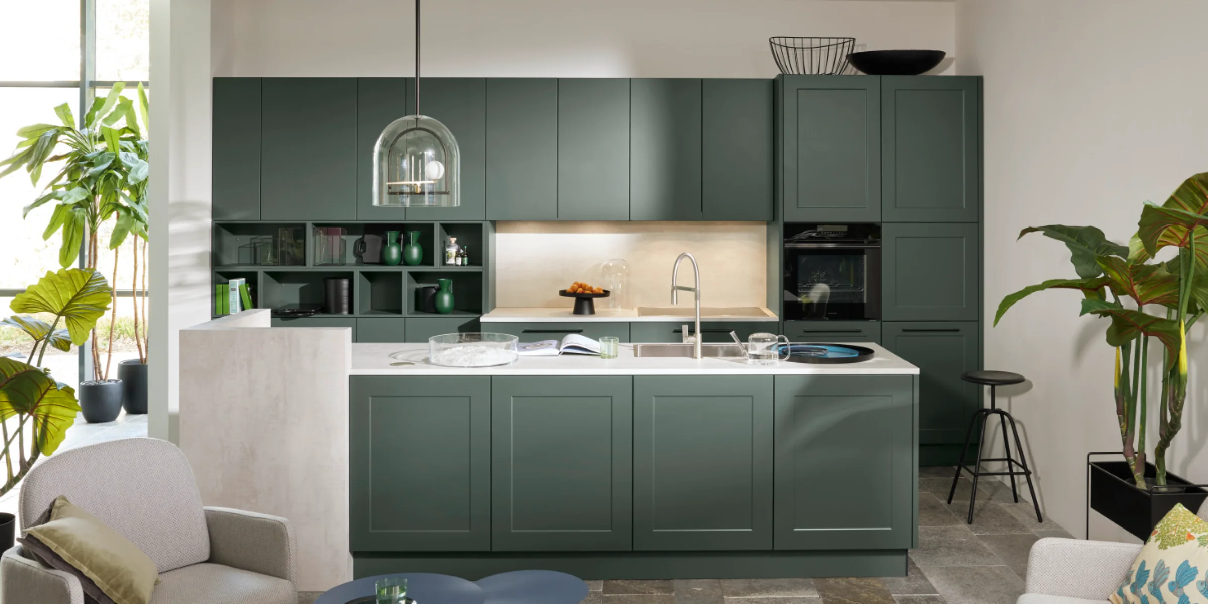 Moderne Nolte Küche mit Kombination aus FRAME LACK und SOFT LACK Fronten in Black Green softmatt, Kochinsel mit Rahmenoptik und heller Arbeitsplatte in Beton Weiß, kombiniert mit gemütlichem Wohnbereich.