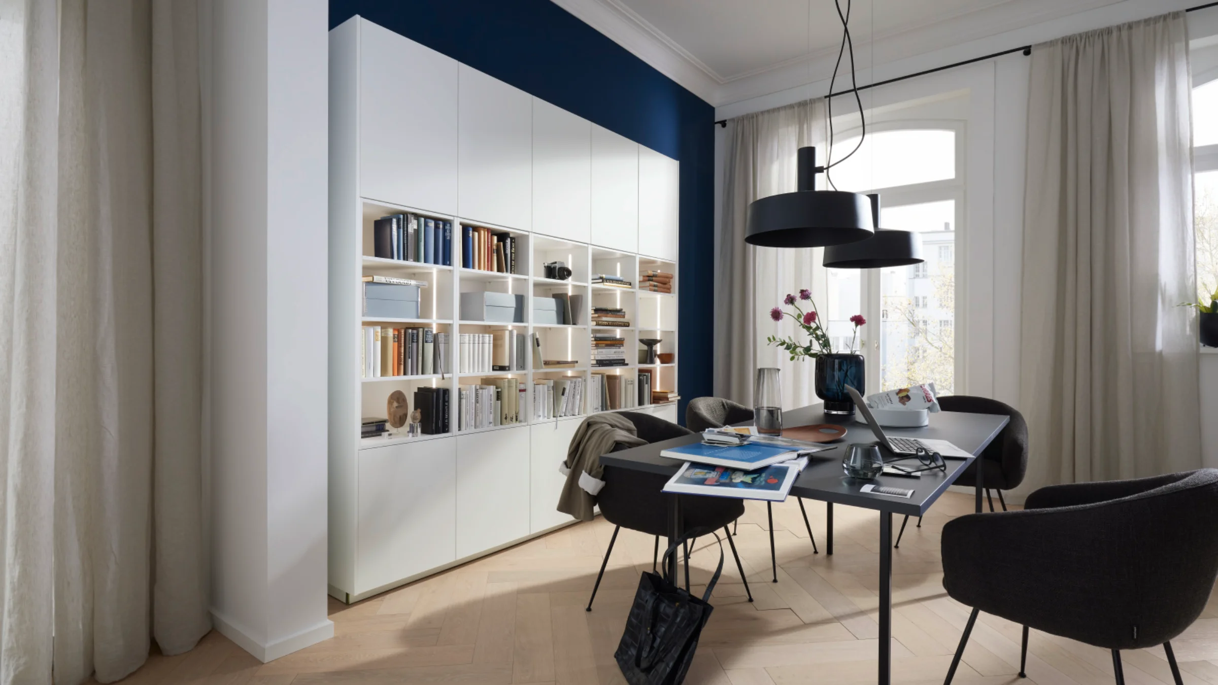 Ein modernes Wohnzimmer mit einem eleganten Bücherregal, Tisch und Stühlen, passend zu Nolte Living.