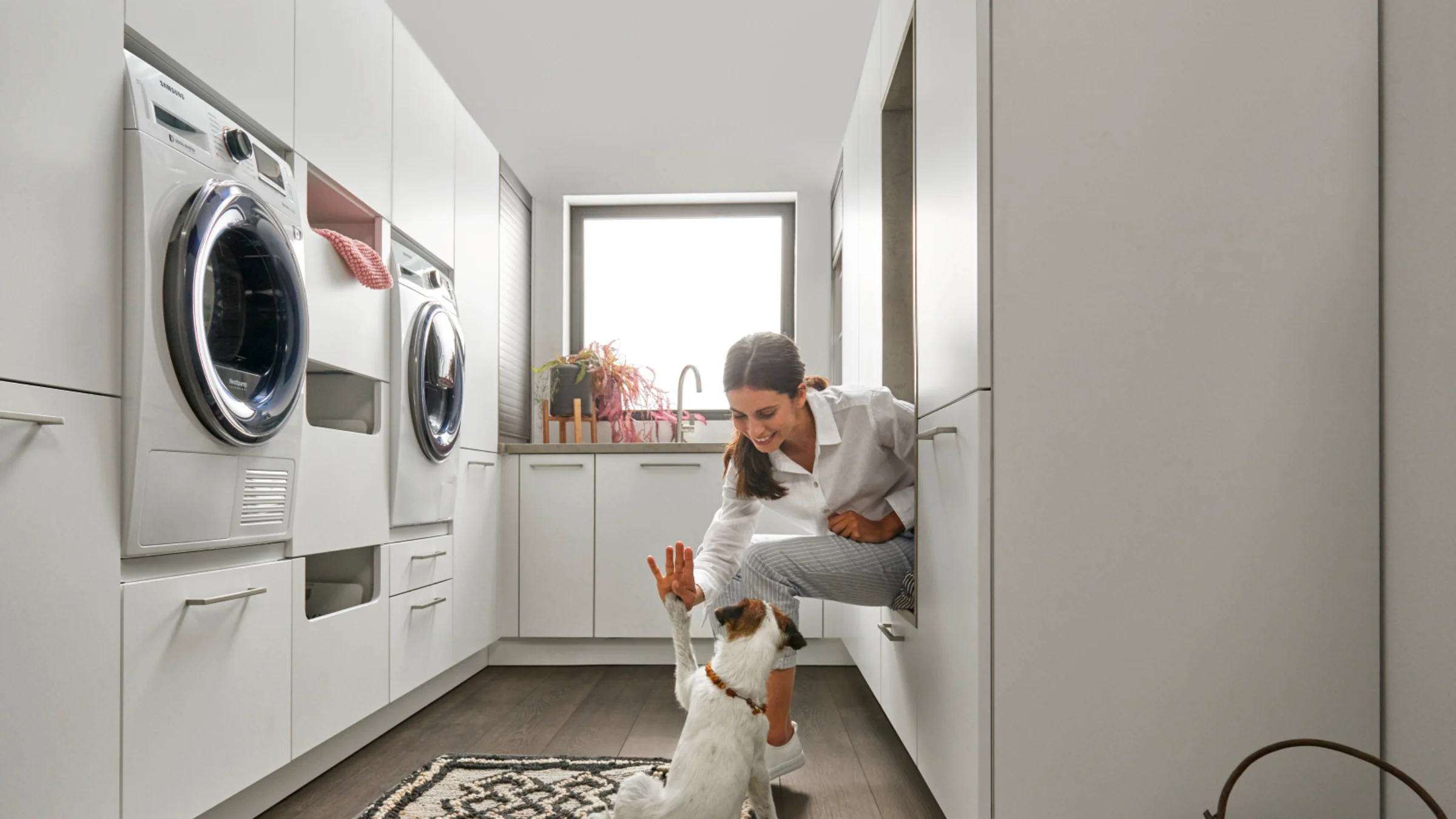 Eine Frau spielt mit einem Hund in einem modernen Hauswirtschaftsraum von Nolte Hauswirtschaftsräume.