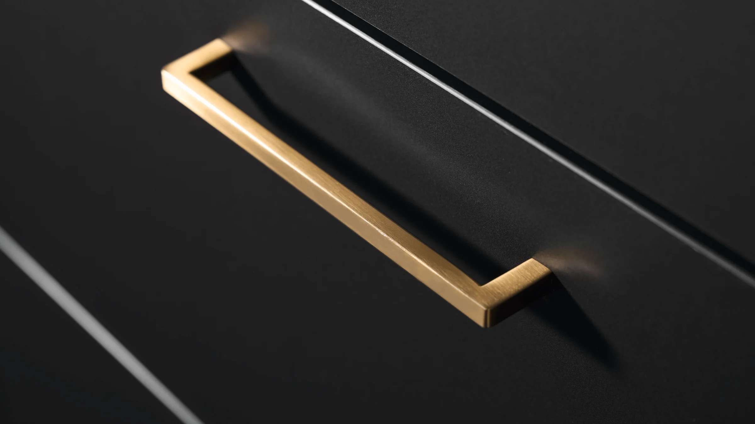 Ein eleganter, goldfarbener Griff ziert eine dunkle Küchenschublade. Express Küchen.