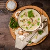 Ein Teller Pilzsuppe mit Petersilie und frischen Pilzen auf einem Holztisch.