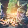 Ein Wanderer geht in Wanderschuhen über einen mit Blättern bedeckten Waldweg.