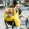 Eine Person trägt einen großen gelben Beutel voller Lebensmittel und schiebt ein Fahrrad.