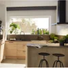 Eine moderne Küche mit Holzschränken und Pflanzen, beleuchtet durch ein großes Fenster. Nolte Küchen.