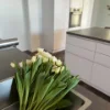 Eine moderne Küche mit weißen Schränken und einem Strauß weißer Tulpen auf der Arbeitsfläche. Nolte Küchen.