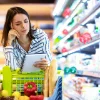 Eine Frau betrachtet nachdenklich eine Einkaufsliste im Supermarkt.