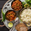 Eine Mahlzeit mit Erbsen-Curry, Reis, Brot, Limette und Gewürzen, appetitlich auf einem Tablett angerichtet.