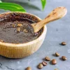 Eine Schale mit Kaffeesatz-Peeling und Kaffeebohnen liegt auf grauem Untergrund.