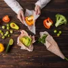 Eine Person wickelt Gemüse in Bienenwachstücher ein, darunter Paprika, Brokkoli und Avocado.