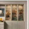 Un aparador elegante con vitrina de vidrio, decorado con vajilla y arte, de Nolte Living.