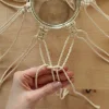 Eine Hand knotet Makramee-Seile um ein Glas auf einem Holztisch.