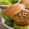 Ein vegetarischer Burger mit Salat und Sprossen liegt auf einem Teller.