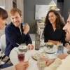 Vier Personen sitzen fröhlich an einem Tisch mit Getränken und Snacks in einem modernen Wohnbereich. Nolte Living.