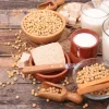 Auf einem Holztisch liegen Sojabohnen, Tofu und Gläser mit Sojamilch.