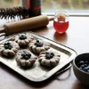 Auf einem Tisch liegen Gebäckstücke mit Blaubeeren, ein Glas Saft und eine Schale mit Blaubeeren.