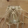 Ein Glasgefäß mit Makramee-Halterung auf einem Holztisch.
