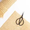 Scissors next to a piece of braided raffia on a white background.