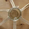 Ein Glas wird von Makramee-Schnüren gehalten, die auf einem Holztisch ausgebreitet sind.