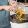 Eine Person entsorgt Gemüsereste in einen Mülleimer in einer modernen Küche von Nolte Küchen.
