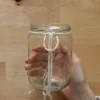 Eine Hand knotet ein Seil um ein leeres Einmachglas.