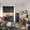 In einem modernen Raum mit grauer Küche von Nolte Küchen sind ein Sofa, ein Schreibtisch und ein elektronisches Schlagzeug zu sehen.