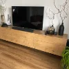 Ein modernes Wohnzimmer mit Holz-Sideboard, dekoriert mit Vasen und Pflanzen, und einem großen Fernseher darauf. Nolte Living.