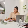 Eine Frau arbeitet an einem Tisch in einem modernen Raum mit offener Küche im Hintergrund von Nolte Küchen.