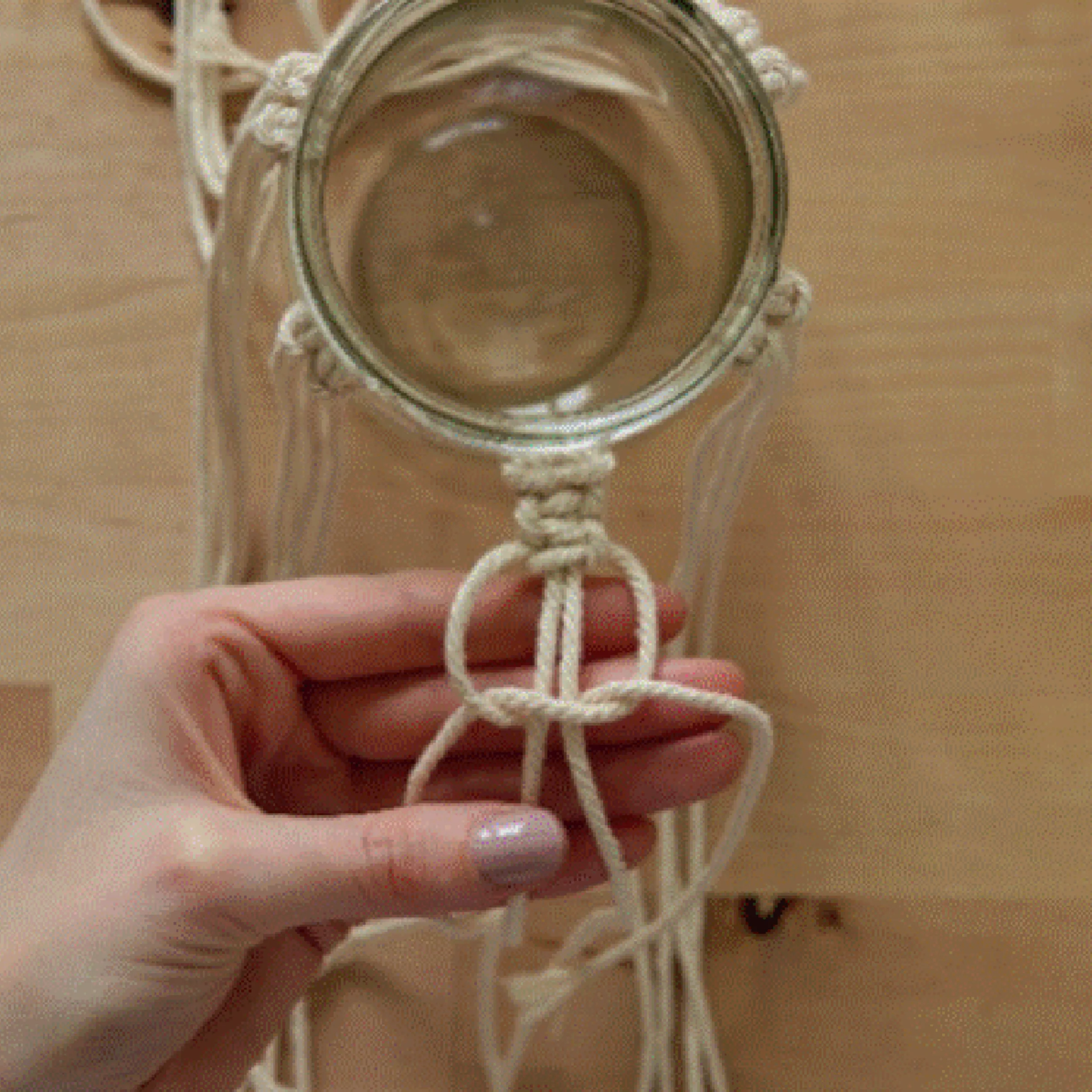 Eine Hand knotet Makramee-Kordeln um ein Einmachglas.