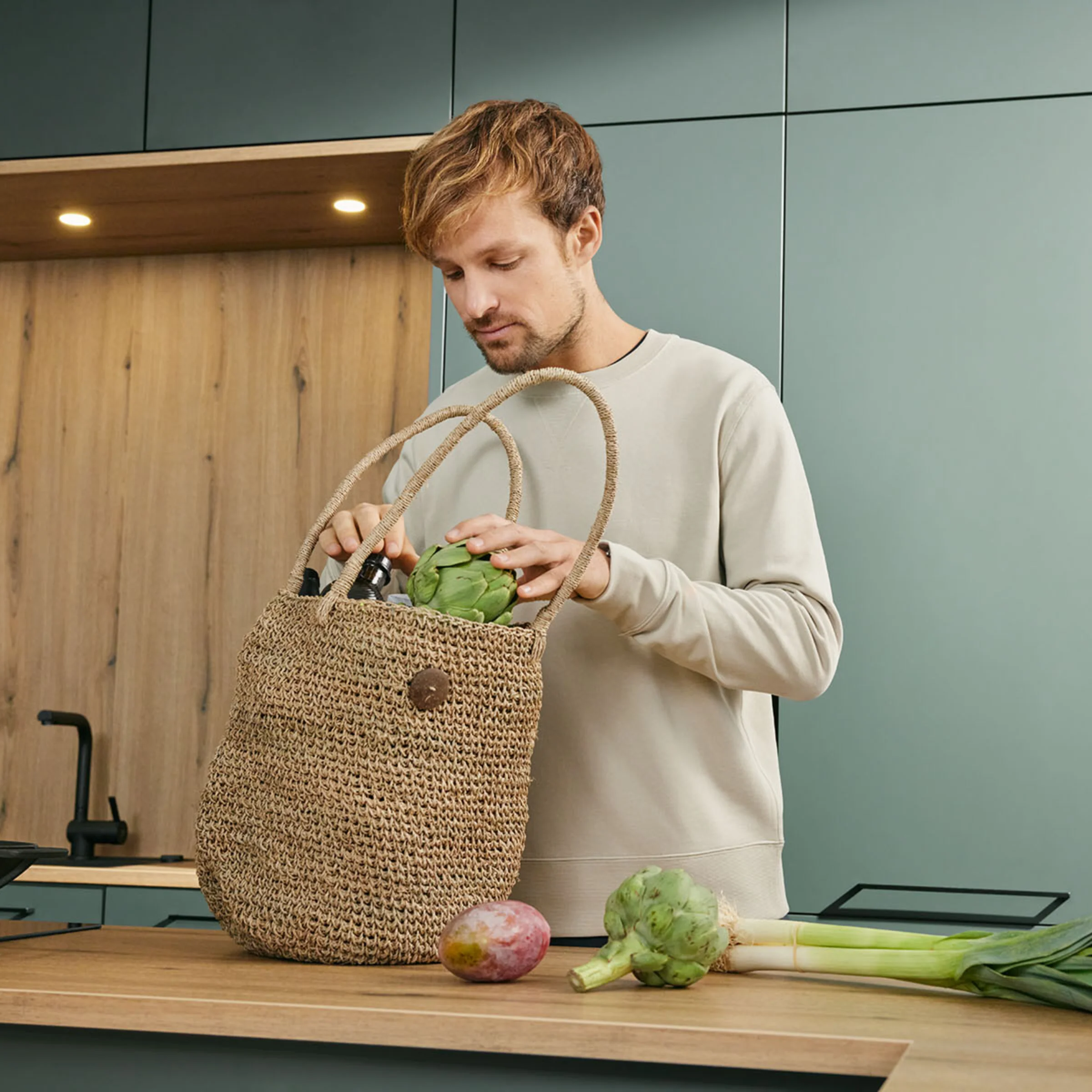 Ein Mann steht in einer modernen Küche von Nolte Küchen und räumt Einkäufe aus einer Jutetasche auf die Arbeitsplatte.